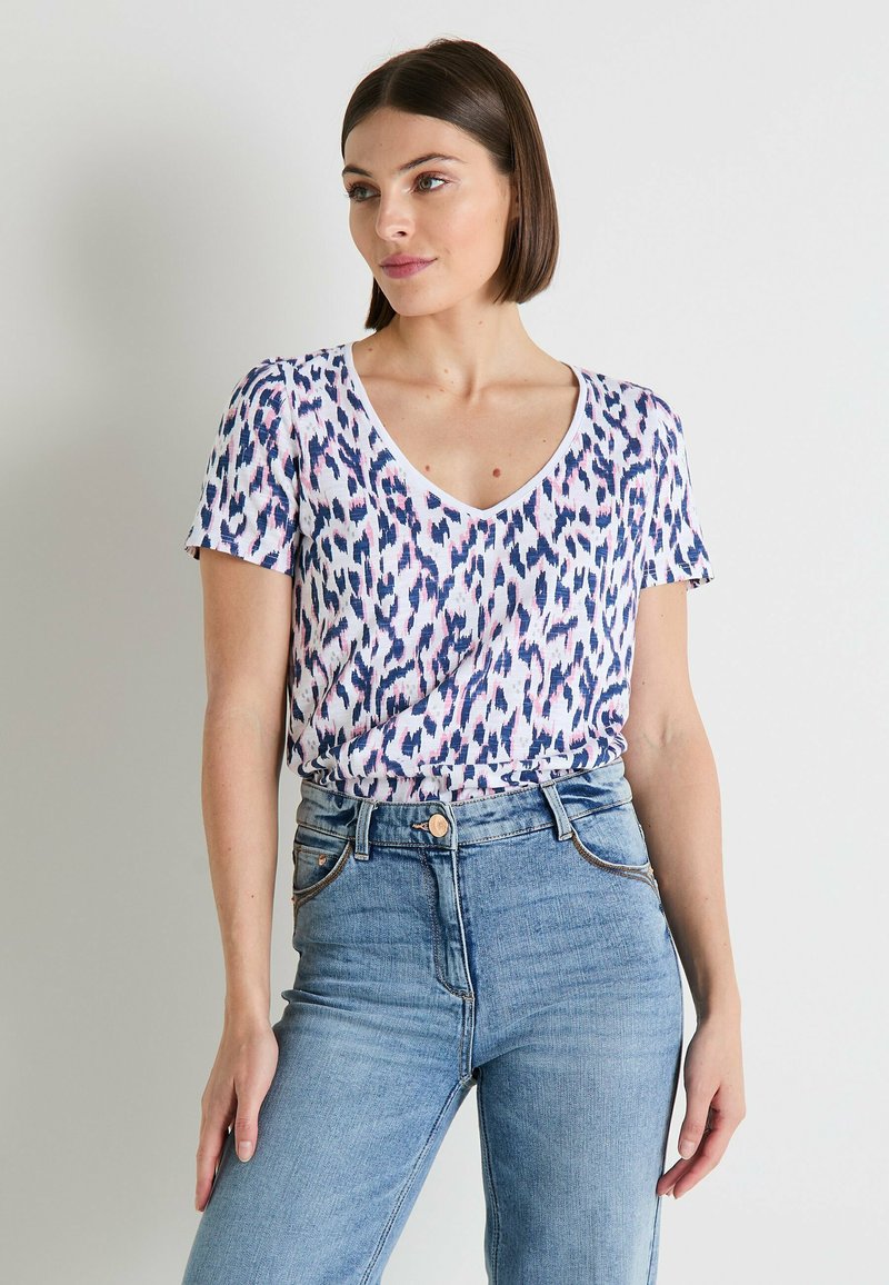 Camiseta de manga corta con escote en V en color rosa, azul marino y blanco con un estampado de leopardo; combinada con jeans azules de cintura alta.
