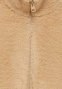 Veste en polaire beige avec fermeture éclair verticale, surface texturée et col haut. Tissu doux et pelucheux, conçu pour la chaleur.