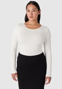 Långärmad vit topp med rundad halsringning, slät textur, figursydd design; matchad med en högmidjad svart penskjol.