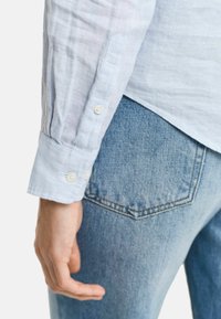 Svetle modrá lněná košile s knoflíkovými manžetami, texturovaná látka, s bílými knoflíky. V páru se světle modrými džíny.