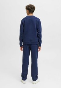 Navy blue sweatshirt with crew neck, ribbed cuffs, and matching joggers. Soft, textured fabric, plain design, worn with white sneakers.