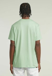 T-shirt in cotone verde chiaro con maniche corte e collo tondo, caratterizzato da una vestibilità rilassata e un design sul retro semplice.