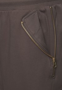 Dunkelgraue Jogginghosen mit einer sichtbaren goldenen Reißverschlusstasche, weichem Material, schmal zulaufendem Bein und elastischem Bund für zusätzlichen Komfort.