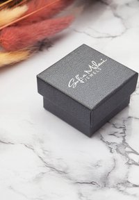 Svart texturerad smyckeslåda med ett gångjärnslock, prydd med ett vitt pr präglat varumärkeslogo "Sofia Milani Jewels." Positonerad på en marmoryta.