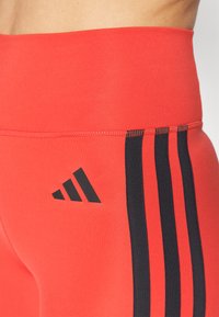 Punased spordileggingsid kõrge vöökohaga. Külgedel on kolm musta triipu ja puusas must logo. Sile tekstuur.