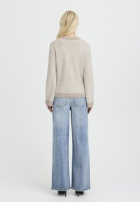 Beżowy sweter z prążkowanego dzianiny z okrągłym dekoltem, zestawiony z jasnoniebieskimi spodniami typu wide-leg. Stylizacja charakteryzuje się luźnym krojem i fakturowanym materiałem.
