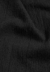 Tissu noir avec une texture ondulée, présentant des lignes verticales en relief. Le matériau semble doux et légèrement brillant, avec un motif homogène.