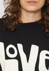 Czarna bawełniana koszulka z dużym, kontrastowym białym napisem "love", z literami w różnych kształtach i okrągłym dekoltem.