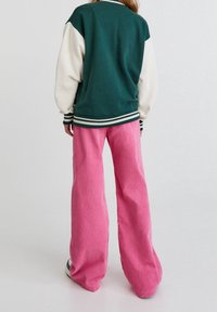 Chaqueta bicolor en verde y crema con puños acanalados, combinada con pantalones anchos de pana rosa. Ambas prendas tienen un corte holgado.