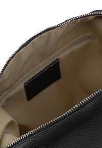 Interior de bolso de cuero negro con una textura suave, forro beige y un bolsillo con cremallera. Presenta una etiqueta cosida y detalles en cremallera plateados.