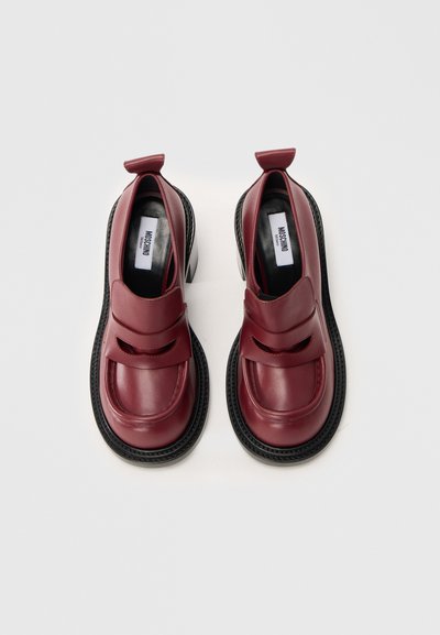 Burgundské kožené boty s kulatou špičkou, černou strukturovanou podrážkou a dvěma výřezy v designu. Obsahují smyčkovou poutko na patě.