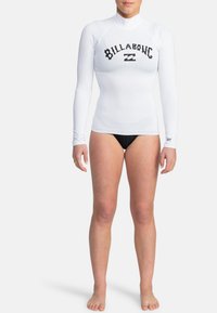 Bílý rash guard s dlouhým rukávem, který na hrudi nese černé logo "Billabong". Vyrobeno z elastického materiálu s designem vzhledem k polo stojáčku.