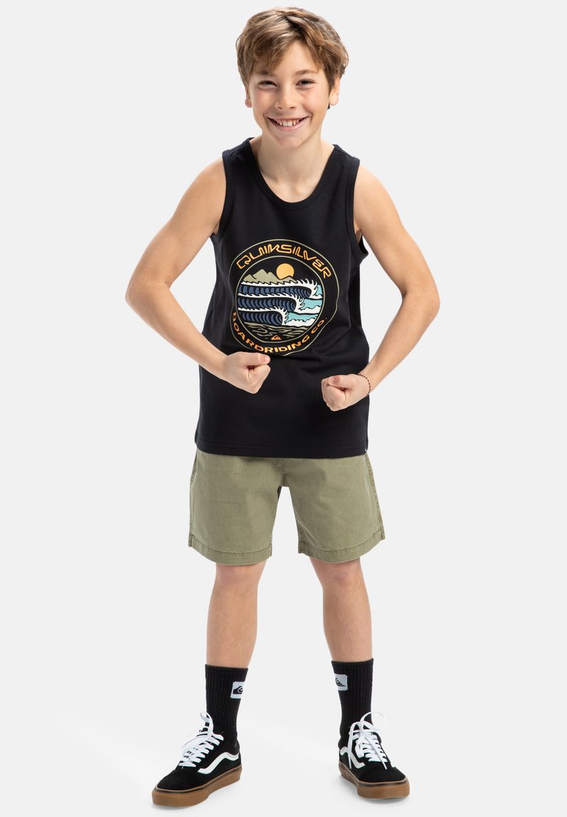 Camiseta sin mangas negra con un gráfico colorido de temática surfer, combinada con pantalones cortos verde olivo, calcetines negros y zapatillas negras.