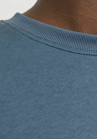 Camiseta de algodón azul con un cuello redondo acanalado y textura suave. El primer plano muestra el detalle de la costura en el cuello y el hombro.