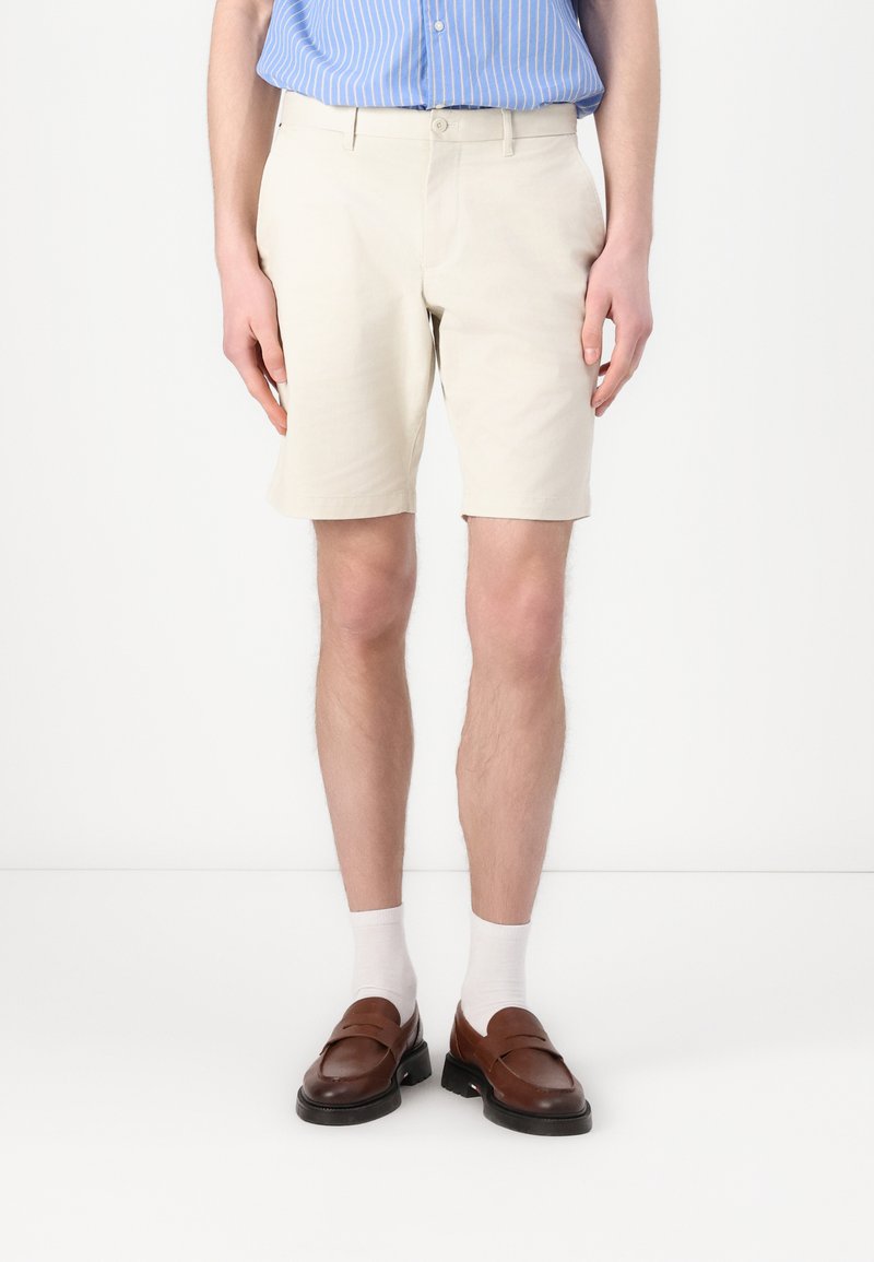 Beige chino shorts, lavet af bomuldsstof, lige snit, frontlommer, båret med brune loafers og hvide sokker, vist på en stående model.