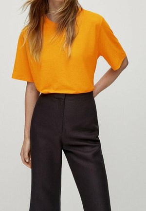 Fel oranje katoenen T-shirt met korte mouwen, gecombineerd met zwarte, wijde broekspijpen en een hoge taille. Gladde textuur en comfortabele pasvorm.