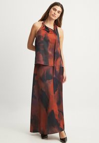 Long dress featuring a halter neck design, made of lightweight fabric with an abstract red, black, and purple pattern. Smooth texture, flowing silhouette.