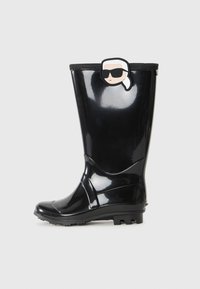 Botte de pluie noire brillante avec un visage de dessin animé portant des lunettes de soleil et une queue de cheval blanche attachée près du haut.