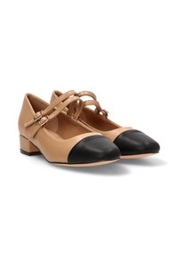 Bailarinas de cuero beige con puntera negra, que cuentan con dos tiras cruzadas en el tobillo con acentos de hardware y un tacón bajo.