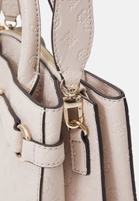 Borsa a mano beige con texture e motivo in rilievo, dettagli in hardware dorato e un bordino nero a contrasto. Presenta due manici e chiusura con zip.
