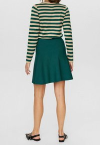 Kermanau panjang bergaris berwarna beige dan hijau dipadukan dengan rok skater biru kehijauan. Rok tersebut memiliki bentuk mengembang dan tekstur kain yang halus.