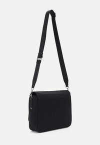 Borsa a tracolla nera realizzata in tessuto resistente, con patta pieghevole, tracolla regolabile e dettagli in metallo argentato. Design minimalista.