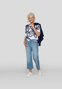 White t-shirt with navy abstract pattern, light blue cropped jeans, and white sneakers; navy sweater draped over shoulder.