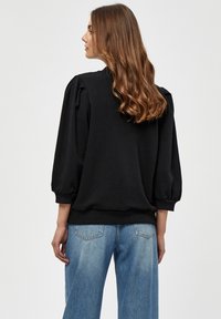 �Črn pulover s napihnjenimi dolgimi rokavi, rebrastimi manšetami in spodnjim robom, v kombinaciji z svetlimi modrimi kavbojkami z visokim pasom. Gladka tekstura tkanine.