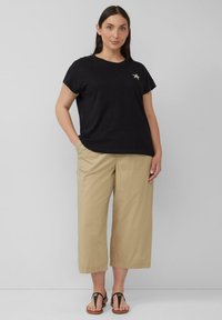 Zwarte katoenen T-shirt met korte mouwen en sterrenborduursel, gecombineerd met beige wijde broek en zwarte flip-flops.