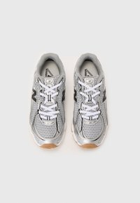 Baskets de sport en maille grises avec des lacets blancs, comportant un accent réfléchissant argenté et une semelle en caoutchouc. Détails de logo remarquables présents.