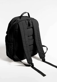 Crni jastučićasti ruksak s dva podesiva remena, gornjom drškom, zatvaranjem na patentni zatvarač i bočnim mrežastim džepovima. Glatka, izdržljiva tekstura materijala.