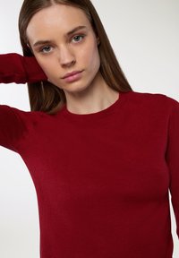 Czerwona sweter dziewiarski z okrągłym dekoltem, długimi rękawami i gładką teksturą. Materiał wydaje się lekki i dopasowany.