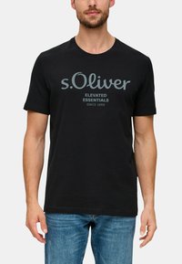 Černé bavlněné tričko s šedým potiskem loga "s.Oliver" a textem "ELEVATED ESSENTIALS SINCE 1969", kulatý výstřih, krátké rukávy.