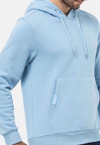 Hellblaue Kapuzenjacke aus weichem Stoff, mit einer frontalen Kängurutasche, einer Kapuze mit Zugband und silbernen Enden.
