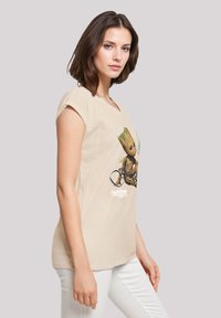 Beige cotton t-shirt with a graphic of a character on a bicycle, short sleeves, relaxed fit, featuring text: "GUARDIANS OF THE GALAXY VOL. 2."