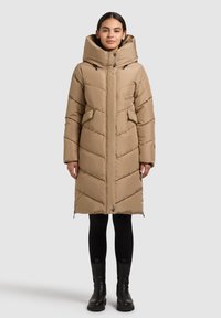 Béžová péřová bunda s vysokým límcem, zipovými kapsami, švem ve vzoru rybí kosti a kapucí se stahovací šňůrkou. Má dlouhé rukávy a boční rozparky.