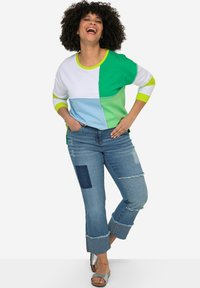 Sudadera de patrón de bloques coloridos en blanco, verde y azul, combinada con unos pantalones vaqueros cortos de color azul claro con parches y bajos deshilachados.