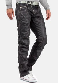Jean noir en denim, avec des coutures blanches contrastantes, plusieurs poches zippées et un design slim.