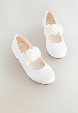 Weiße Satin-Balletschuhe mit einer runden Spitze und einem Riemen, der mit zwei weißen Blumenverzierungen geschmückt ist. Flache Sohle, schlichtes Design.