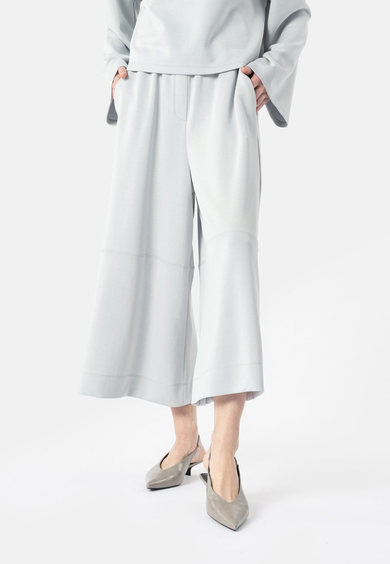Pantalon gris clair à jambes larges associé à des escarpins slingbacks à bouts pointus, porté avec les mains dans les poches et un haut assorti gris clair.