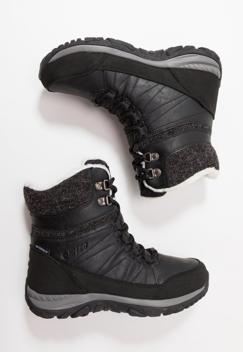 Botas impermeables negras con parte superior de cuero, forro de lana, suela de goma gris y un prominente detalle de cordones para un ajuste seguro.