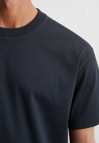Granatowa koszulka z okrągłym dekoltem, wykonana z miękkiej bawełnianej tkaniny, z krótkimi rękawami i gładką fakturą z subtelnymi detalami przeszycia.