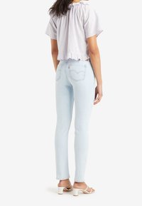 Světle modré skinny džíny se středně vysokým pasem, s klasickým pětipocket designem a jemným prošíváním. V kombinaci s levandulovým crop topem.