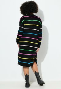 Schwarzes Strickkleid mit mehrfarbigen horizontalen Streifen, langärmlig und mit seitlichen Schlitzen, kombiniert mit schwarzen plateau-besetzten Stiefeln.