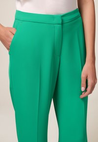 Groene, high-waisted broeken van een gladde stof met een tailored fit. Voorzien van zijzakken en een strakke, rechte silhoutte.