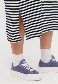 Randig svart och vit midi-klänning med sidslits, matchad med lila mockasneakers och vita ribbade strumpor.