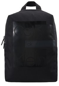 Sac à dos en tissu noir avec poignée supérieure, poche avant zippée et logo Calvin Klein discrètement embossé.