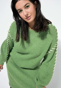Grüner, oversized gestrickter Pullover mit strukturiertem Finish, der weißem Garnakzent an den Ärmeln und einem gerippten Kragen verfügt.