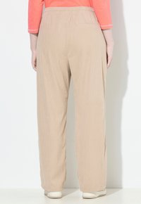 Beige manžestrové kalhoty s uvolněným střihem, které mají široký pas a jemnou vroubkovanou texturu. Obsahují detail zadní kapsy.