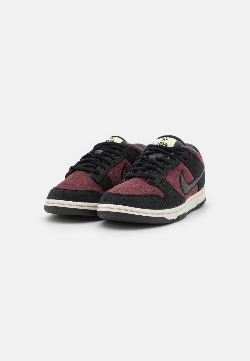 Schwarze und kastanienbraune Sneaker mit Veloursledertextur, schwarzen Schnürsenkeln und einer weißen Zwischensohle. Enthält ein Logo an der Seite und ein leuchtend grünes Zungenlabel.